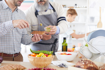 Close-up of young man standing and tasting sauce giving by the mature man while they preparing food in the kitchen