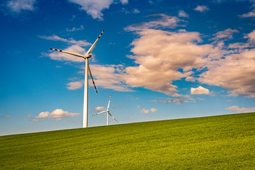 Wind turbines in the green field with blue sky and clouds