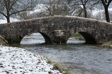 Fototapeta na wymiar un vieux pont jura en pierre médiéval en hiver avec neige et rivière