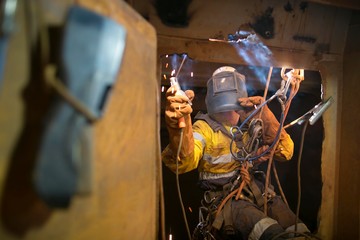 Rope access welder wearing fully safety uniform fall protection helmet, welding glove harness, commencing welding chute repair in confined space construction mine site Perth Pilbara region Australia