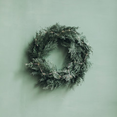 Christmas / New Year composition. Festive wreath made of christmas tree, fir branches against pale green wall. Minimal winter holidays concept. © Floral Deco