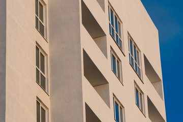 part of the white facade of the building with windows and balconies against a clear blue sky at sunrise and sunset