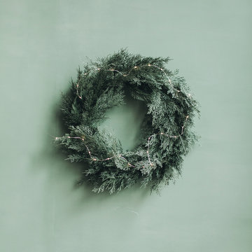 Christmas / New Year Composition. Festive Wreath Made Of Christmas Tree, Fir Branches Against Pale Green Wall. Minimal Winter Holidays Concept.