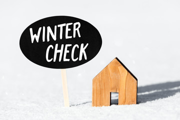 Kleines Haus steht im Schnee, Schild mit Text Winter Check, Eigenheim winterfest machen