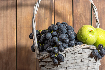 green apples and red grapes in basket on wooden background, autumn harvest with copy space