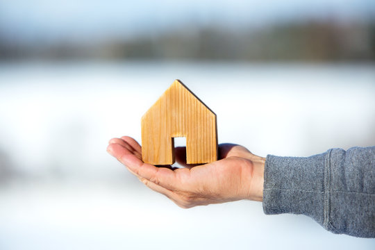 Hand h&auml;lt ein Haus, im Hintergrund ist freie Baufl&auml;che