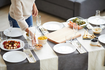 Close-up of woman putting the meal on the served table and preparing for the dinner in domestic room