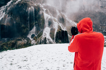 un homme visitant une cascade gelée dans le jura.  Un touriste photographiant une cascade gelée.