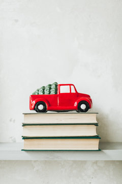 Christmas / New Year composition. Traditional toy of christmas red car with fir on the roof standing on books. Minimal winter holidays concept. Christmas card.