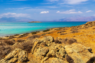 picturesque rocks in savannah with beautiful golden gtass on a coast, green bushes with beautiful turquoise sea , deep blue  sky with clouds and mountains on background, desert landscape