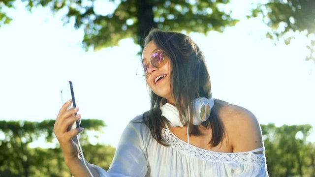 Teenager sharing photograph on social media with mobile phone girl with headphones and sunglasses Teenager making selfie