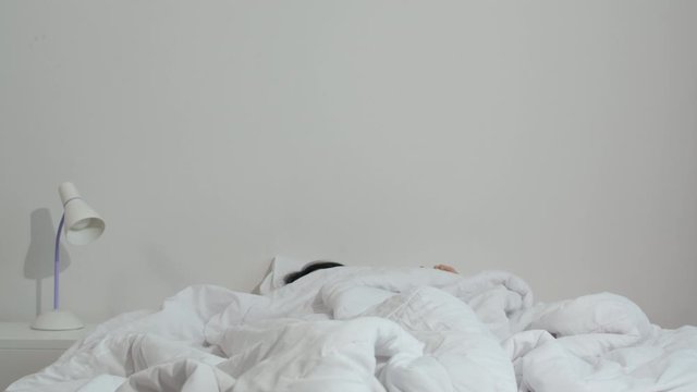 Sleepy Asian young woman shocked as he wake up late for an appointment on bed in bedroom at home in morning. Indian female missed ringing of alarm clock in mobile phone and have overslept awakening.