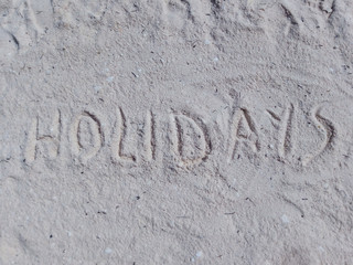 the word "holidays" written on the sand of a beach.