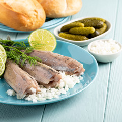 Traditional dutch food freshly salted herring fish with onion called hollandse nieuwe on turquoise plate and wooden background. European food concept with copy space.