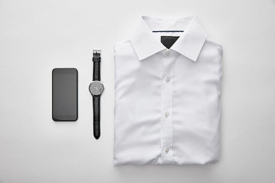 flat lay with plain white folded shirt near smartphone and watches on white background