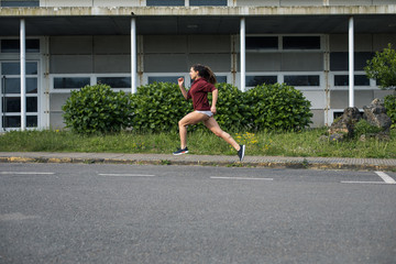 Side view of female athlete running with good technique on asphalt road. Sporty woman in shorts training outside.