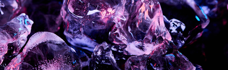 panoramic shot of transparent ice cubes with purple colorful lighting isolated on black