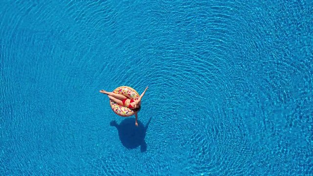 Aerial view of a woman in red bikini lying on a donut in the pool