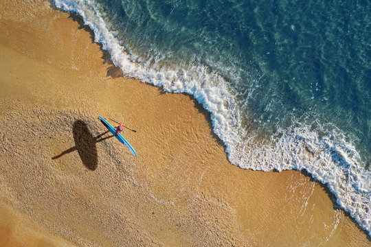 Surfer on beach with paddleboard. Aerial view.