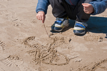 Baby draws on the sand with a wooden stick on a winter day. Children's games. Winter dressed child on the beach.
