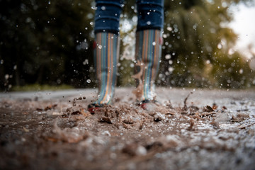 A woman wearing rubber boots jumps into a puddle on a cold autumn day.