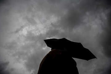 A woman holding an umbrella against a cloudy sky on a cold autumn day.