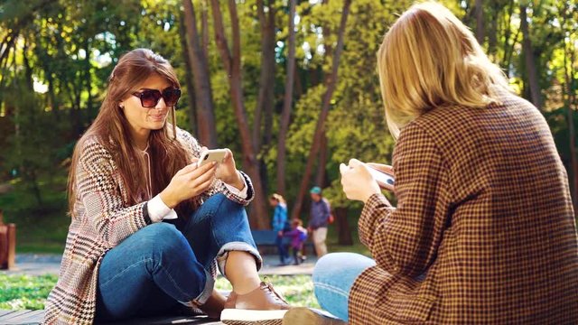 Emotionless girls addicted with smartphones in sunny park