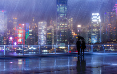 People stand in front of Victoria Harbor, Hong Kong at raining night