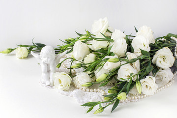 on a white background are white flowers with pearl beads and a ceramic angel figurine