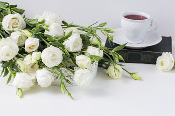 on a white background are white flowers, an old book and a cup of tea