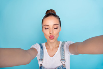 Self portrait of cute charming flirty tempting girl kissing you via camera while isolated with blue background