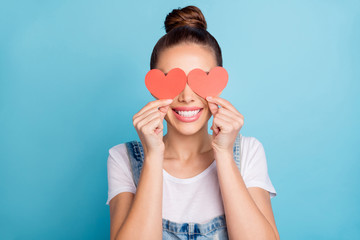 Close up photo of lovely girl hiding her eyes with paper card heart wearing white t-shirt denim jeans overalls isolated over blue background - Powered by Adobe