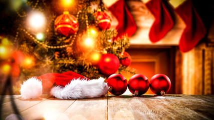 A wooden table with space for your advertising products. Blurred great green Christmas tree and Fireplace with flames and red socks of Santa Claus background.