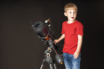 Fototapeta na wymiar A little boy in red football is standing next to a large telescope.