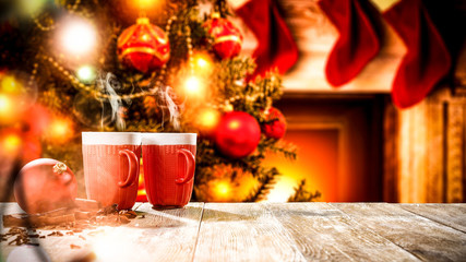 A wooden table with space for your advertising products. Blurred great green Christmas tree and Fireplace with flames and red socks of Santa Claus background.