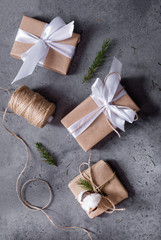 Fototapeta na wymiar gift boxes wrapped in Kraft paper, with white ribbon and rope, silver balls, reel with rope, spruce branches on a gray background, top view