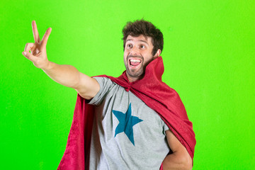 Young crazy super hero making a victory gesture, feeling happy, positive and successful over green...