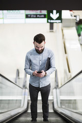 Low angle view of a young businessman standing on escalator using mobile phone