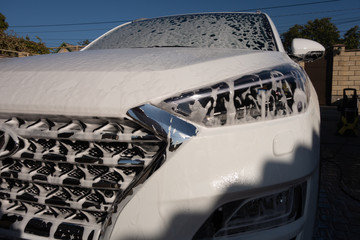 A middle-aged man teaches children of boys 4 and 10 years old to wash a car in the yard of his...
