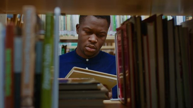 Young black man choosing book in public library