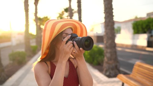 Photographer tourist woman in a big yellow hat taking photos with camera in a beautiful tropical landscape at sunset