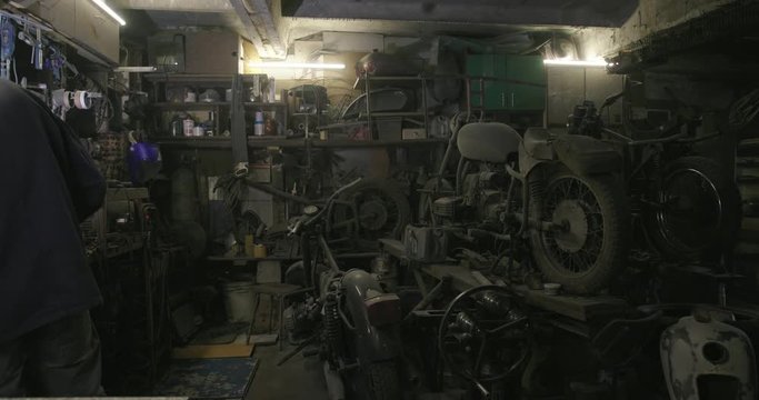 An experienced biker will weld a motorcycle part in his old dusty garage against the backdrop of old vintage motorcycles.