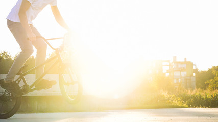 Close up of young unrecognizable man BMX biker jumping bunny hop tricks on summer afternoon with lens flare