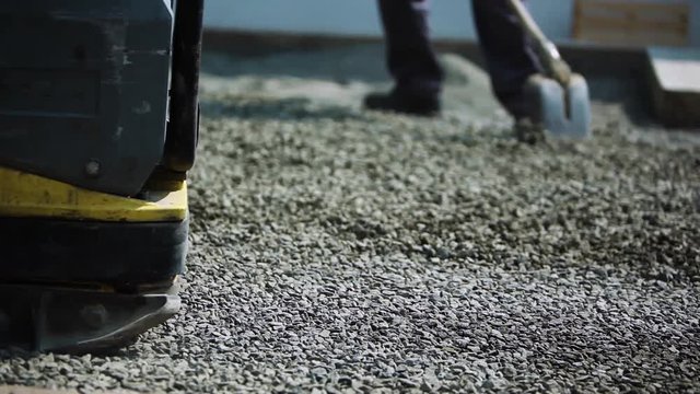 Stone Pavement Road Construction Workers. Leveling The Sand Layer using a finishing plate compactor