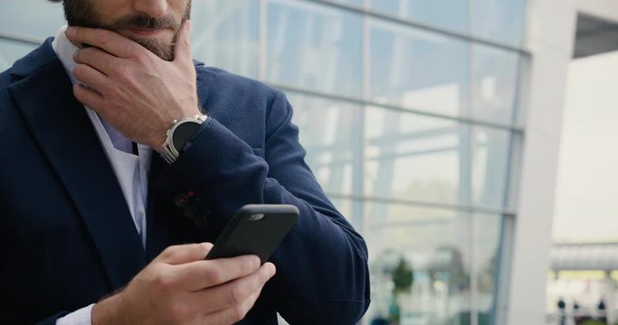 Closeup of Bearded Businessman is using his Smartphone while texting Messages. Professional Businessman is wearing classical Suit and Watches. Serious Business. Social Network. News. Apps.
