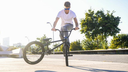CLOSE UP Extreme bmx biker riding in sunny park stopping the bmx bike and doing nollie tail whip...