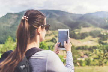 Woman hiker with backpack using blank screen tablet device. Nature landscape in the background.