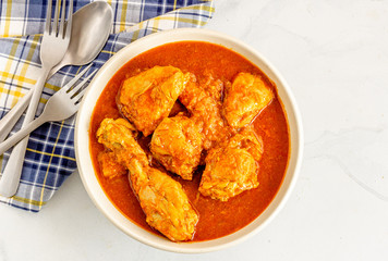 Indian Chicken Curry in a Bowl with Fork and Spoon on White Bacground Directly Above Photo.