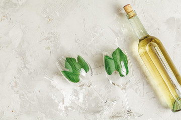 Creative food art background. Bottle of wine and two wineglasses with green grape leaves, top view,...