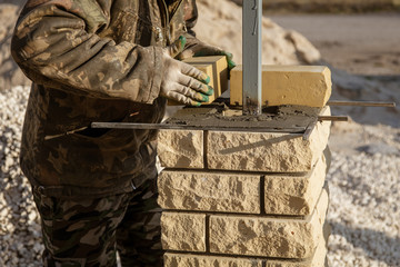 The worker is laying bricks on the fence